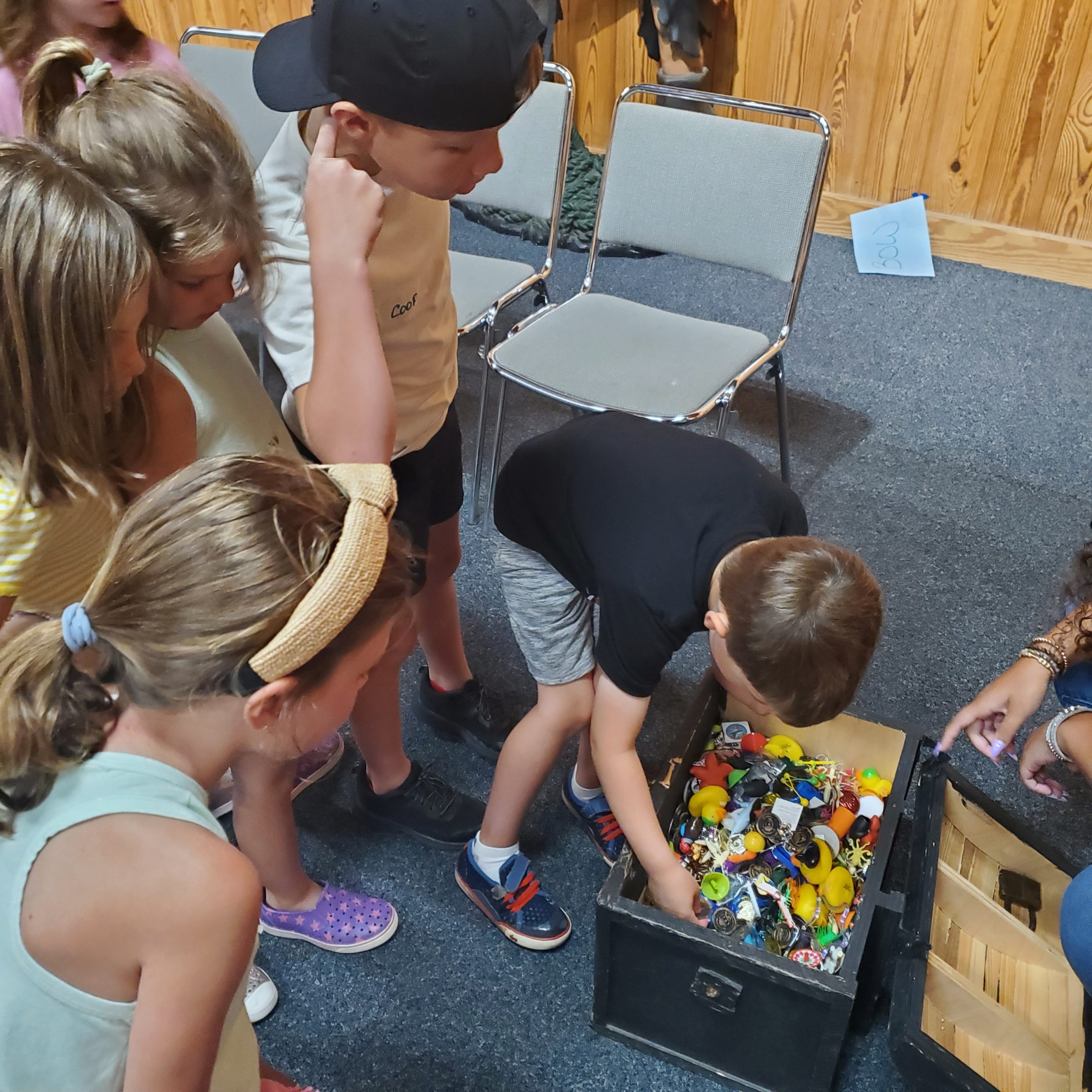 Children surround a boy picking a small toy out of a treasure chest