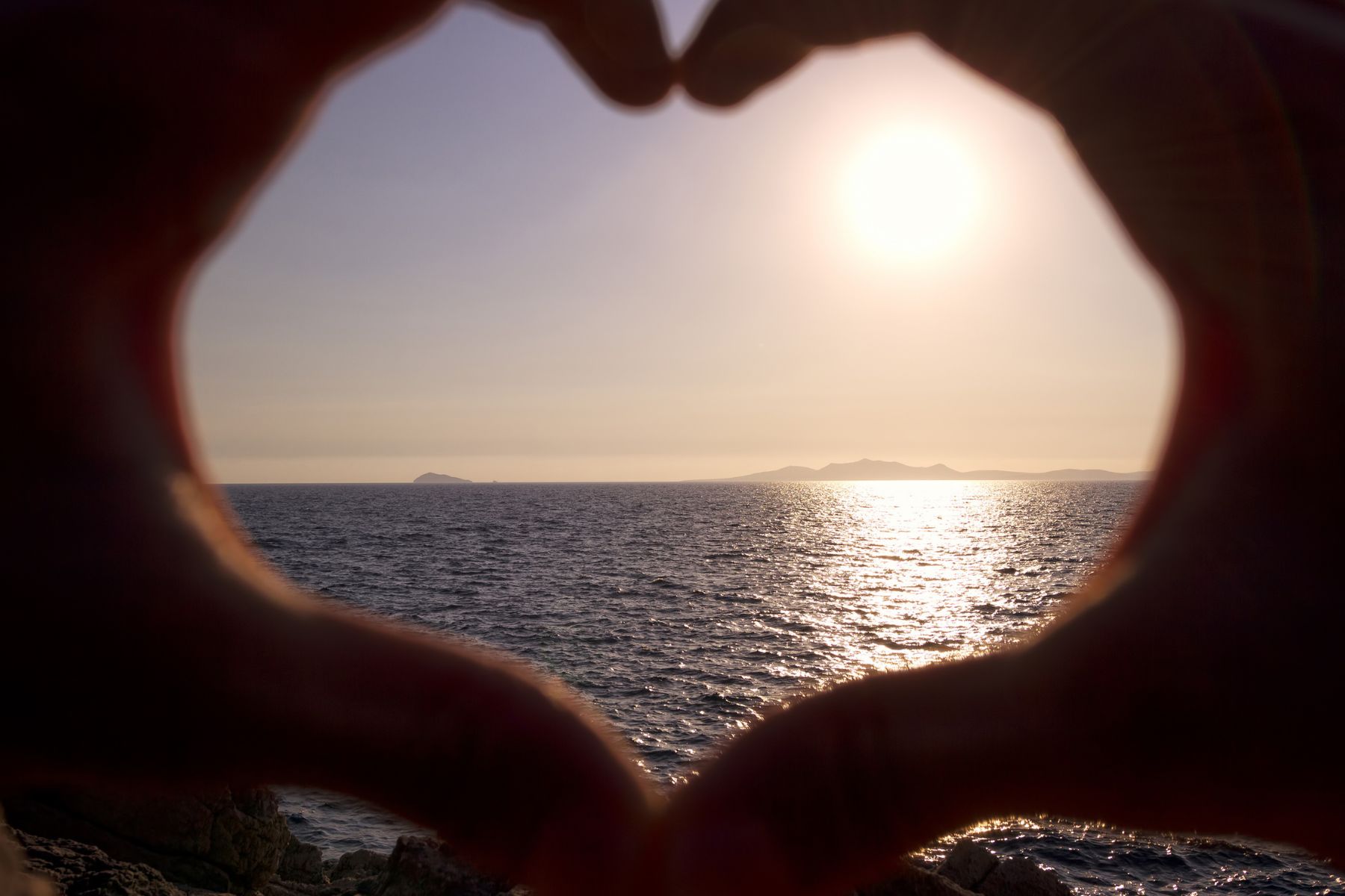 two hands making the heart shape with the ocean in the background