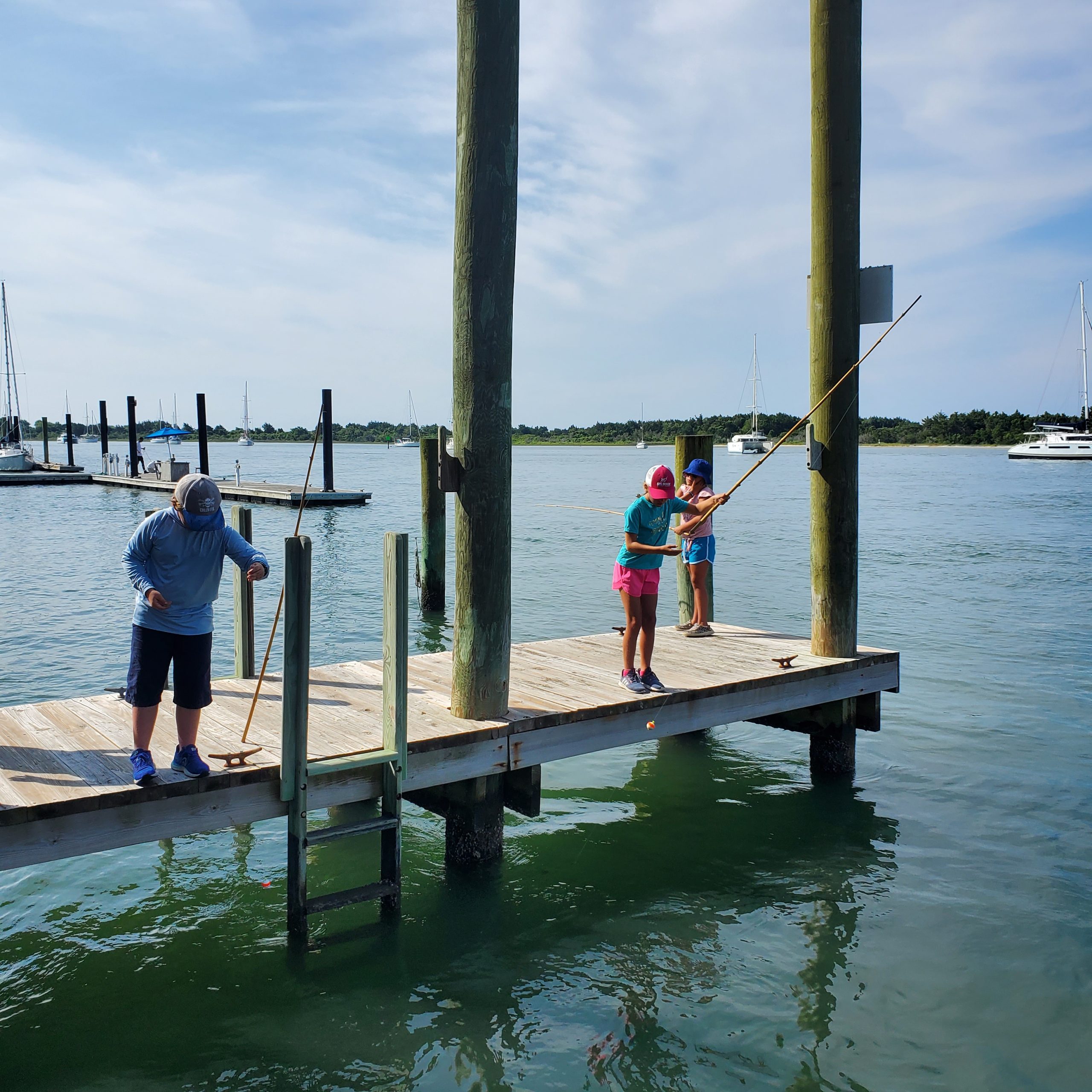 three children fish with cane poles off a fixed dock